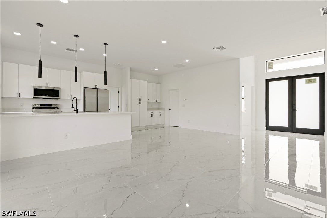 532 Lone Star Lane, Lehigh Acres, FL 33974 Open-concept living area featuring polished tile flooring, white shaker-style cabinetry, stainless steel appliances, and a kitchen island with pendant lighting