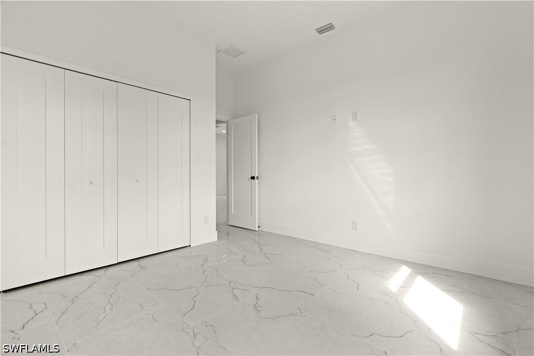 532 Lone Star Lane, Lehigh Acres, FL 33974 Spacious bedroom featuring polished stone-finish flooring with elegant veining, floor-to-ceiling built-in closet cabinetry with white panel doors, abundant natural light from expansive windows, and clean white wall finishes throughout