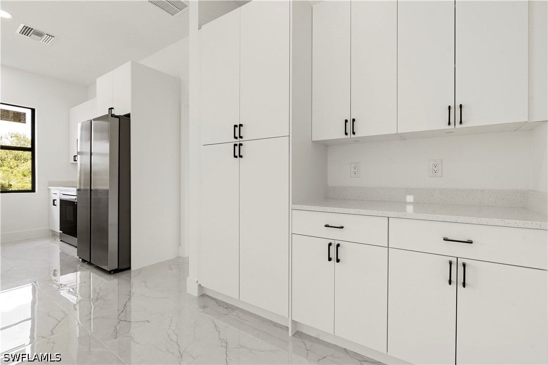 532 Lone Star Lane, Lehigh Acres, FL 33974 White shaker-style cabinetry with matte black hardware, stainless steel refrigerator, white quartz countertops, and polished tile flooring