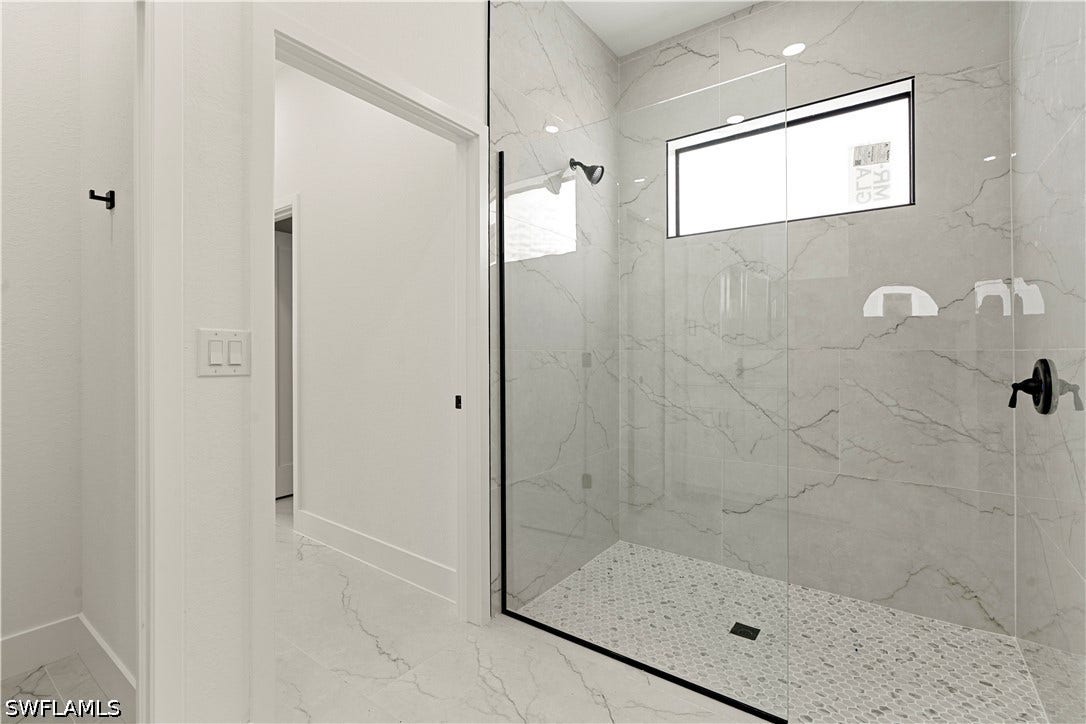 532 Lone Star Lane, Lehigh Acres, FL 33974 Spacious shower with clear glass enclosure and black hardware, featuring a transom window, large format tile walls, and a tiled shower floor