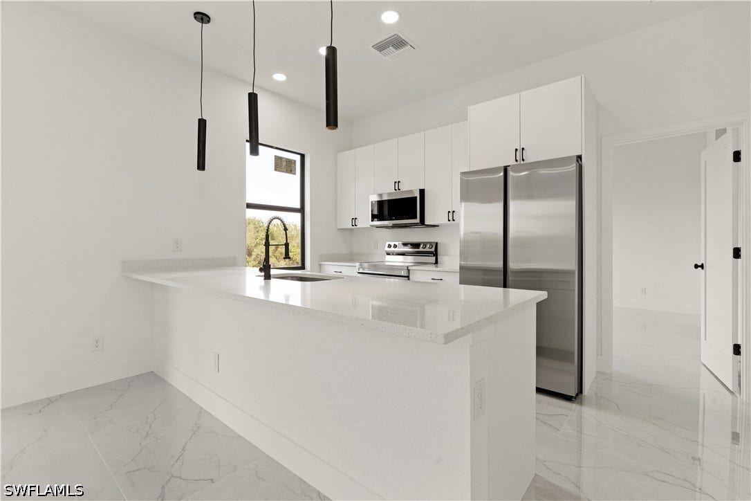 532 Lone Star Lane, Lehigh Acres, FL 33974 Central kitchen island with a built-in sink, white cabinetry, stainless steel appliances, and white tile flooring