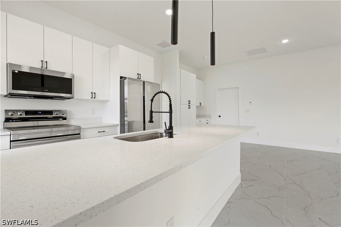 532 Lone Star Lane, Lehigh Acres, FL 33974 Kitchen featuring white cabinetry, stainless steel appliances, a large island with a sink, and pendant lighting