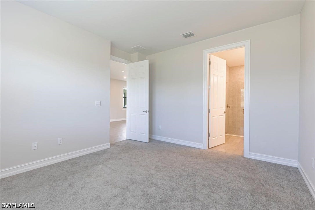 Unfurnished bedroom featuring light carpet and connected bathroom