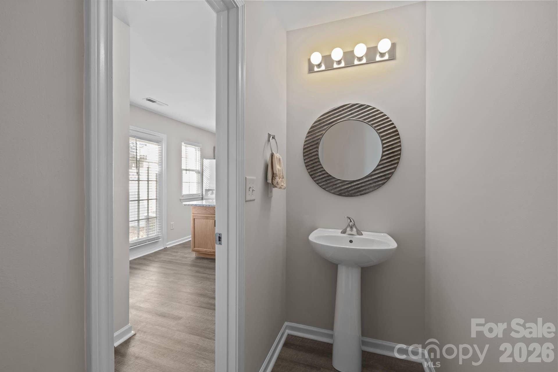 Half bath behind the kitchen with decorative mirror and pedestal sink.