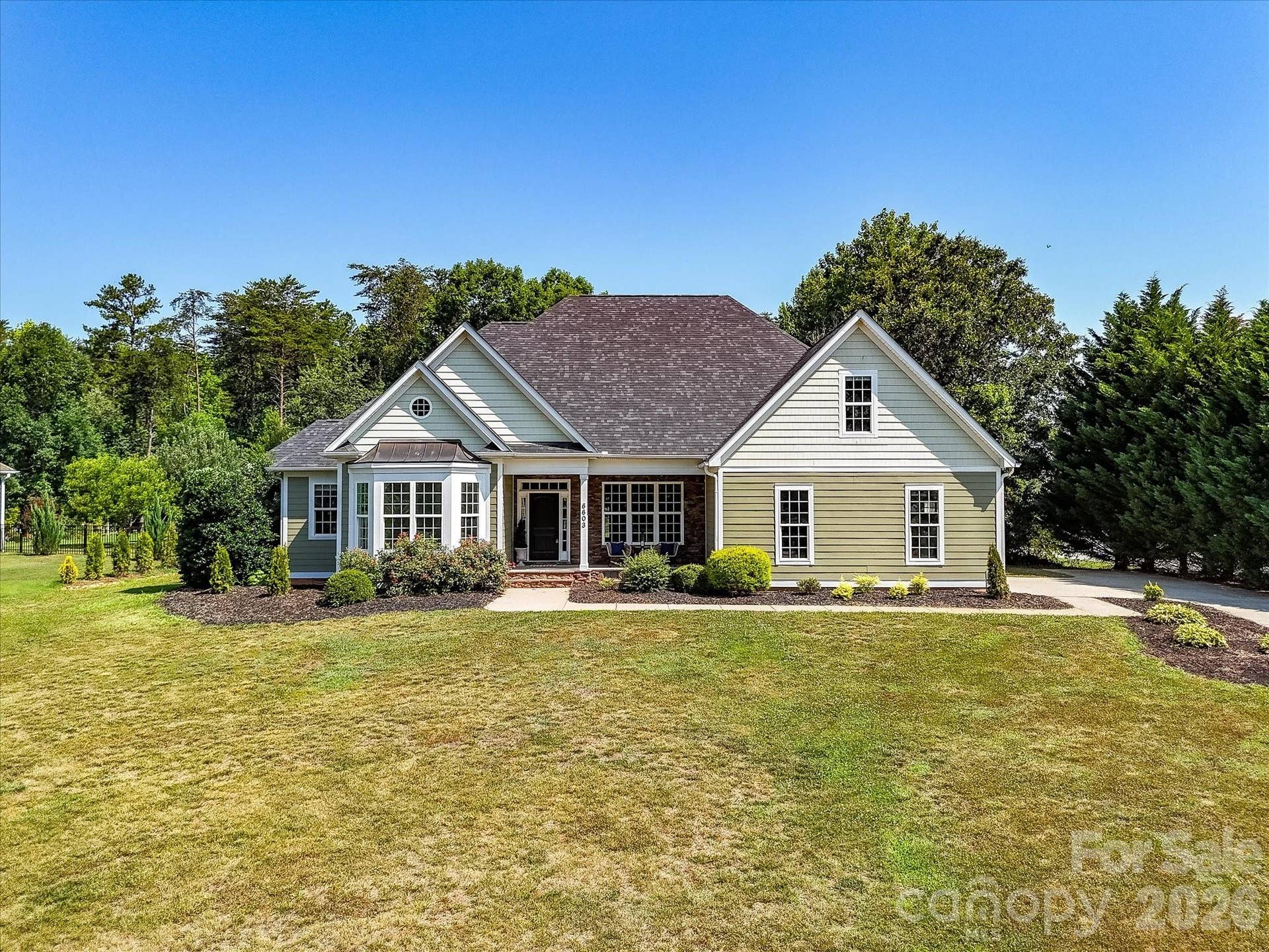 The charming front elevation showcases timeless curb appeal with professional landscaping, a welcoming covered porch, and an oversized homesite surrounded by mature trees.