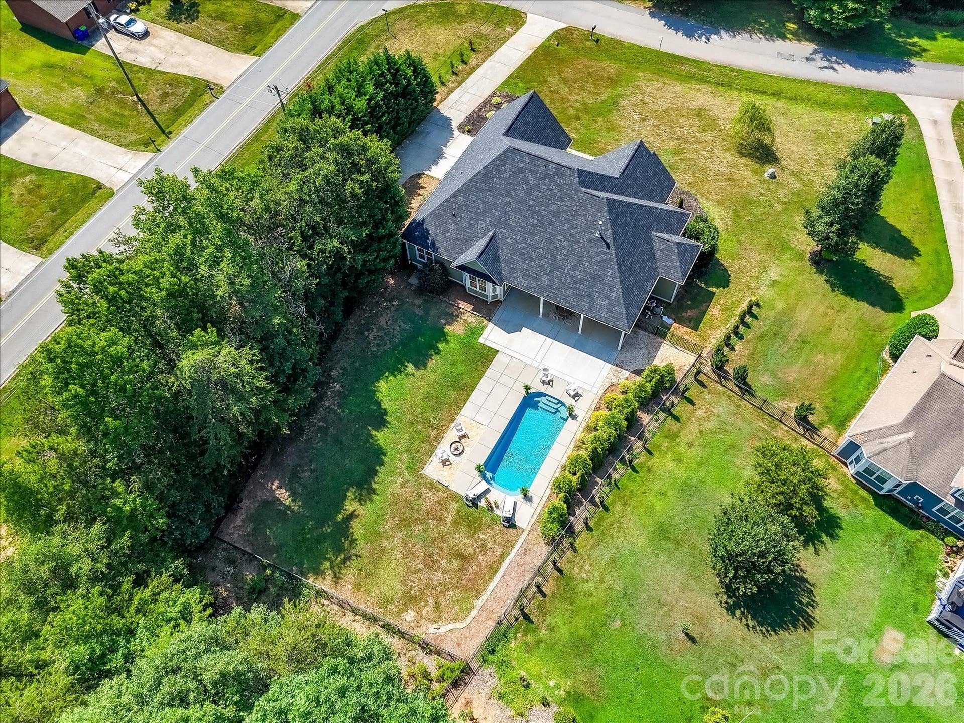 The aerial view highlights the home's private setting with a resort style pool, covered patio, expansive backyard, and mature trees surrounding the property.
