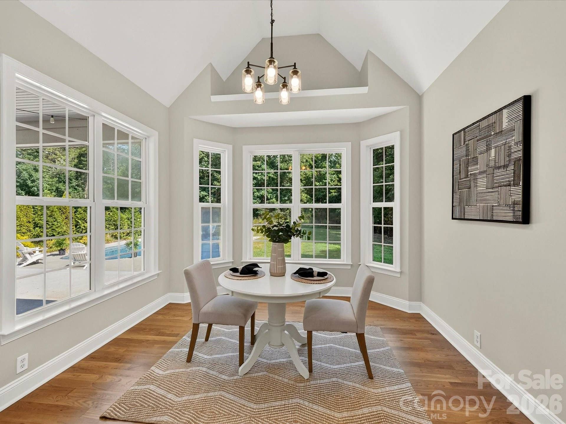 The bright breakfast nook features vaulted ceilings, a wall of windows overlooking the backyard and pool, and an inviting space for casual dining filled with natural light.