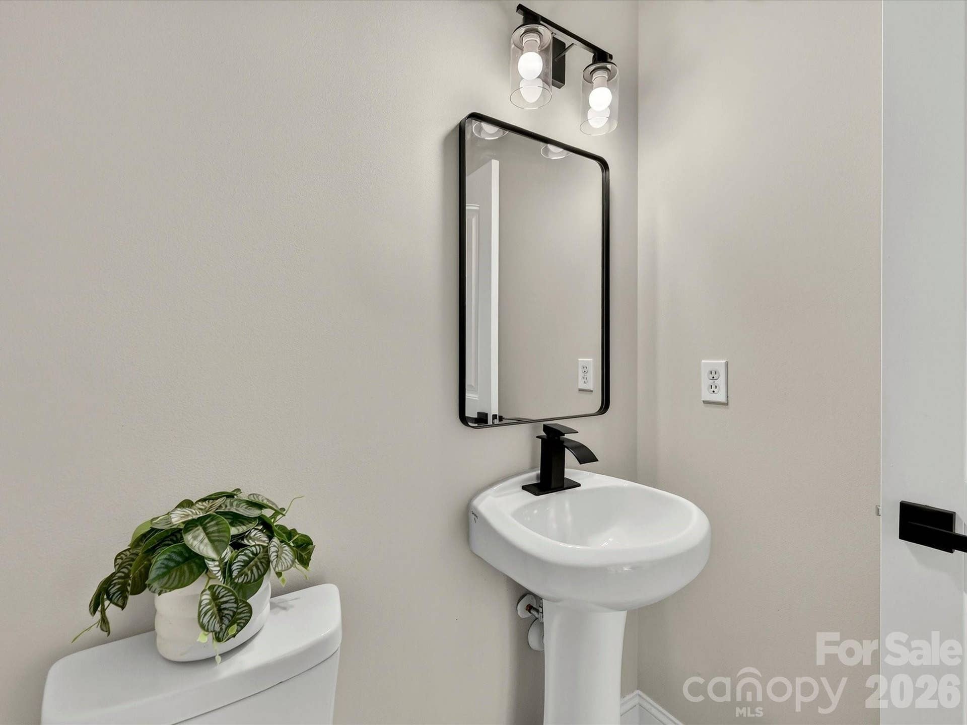 The stylish powder room features a modern pedestal sink, updated black fixtures, and a clean contemporary design that is perfect for guests.