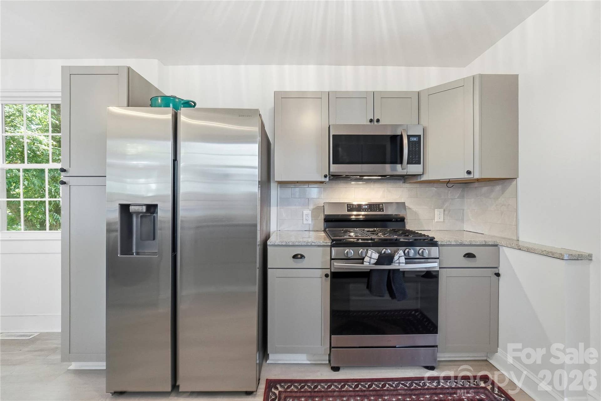 Stainless steel appliances, including a gas range, refrigerator, and microwave, sit against a clean subway tile backsplash.