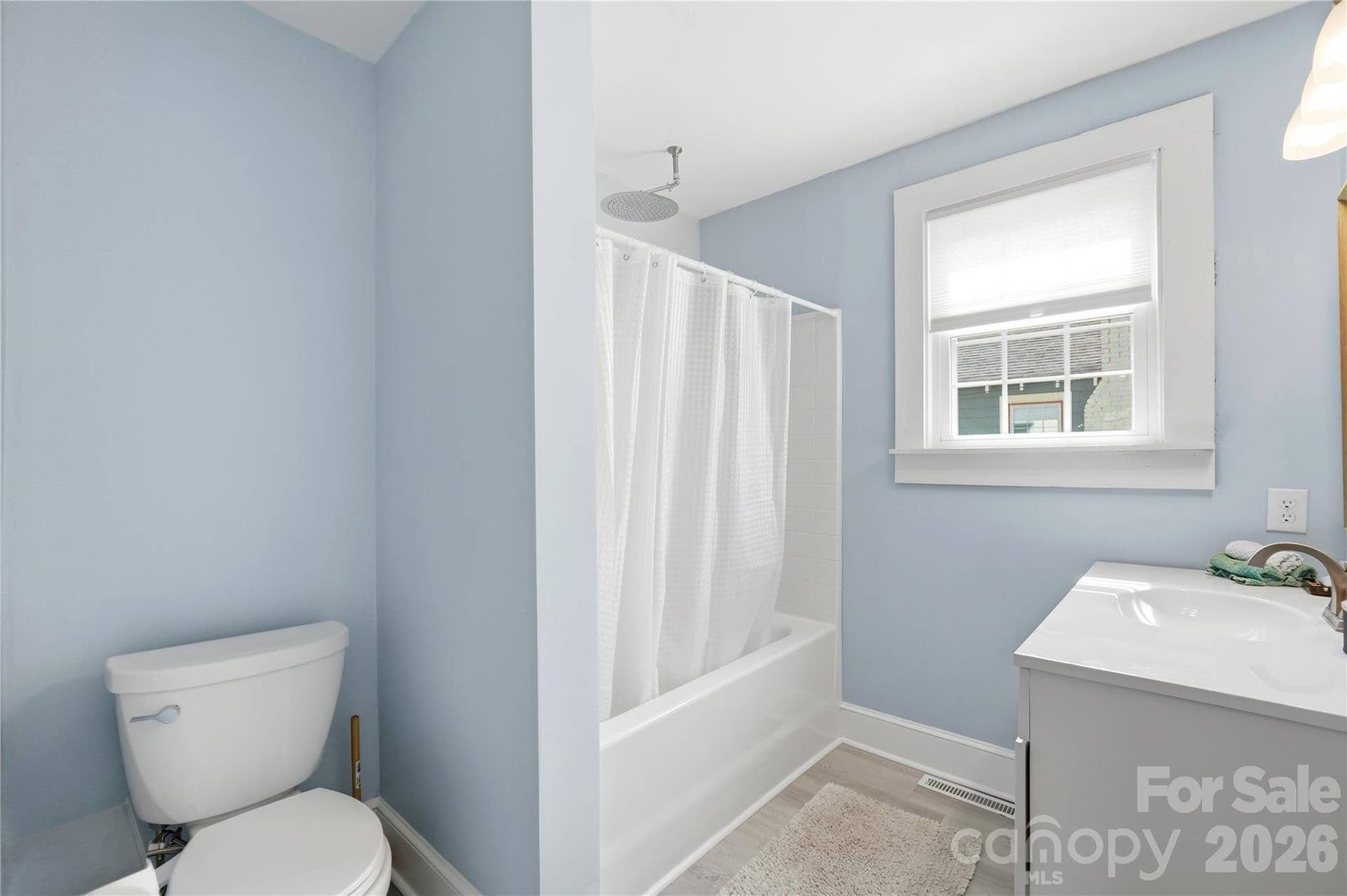 A bathroom refresh done right. This bathroom features a new vanity and a rainshower head above the tub, with a calming color palette and natural light from the window.