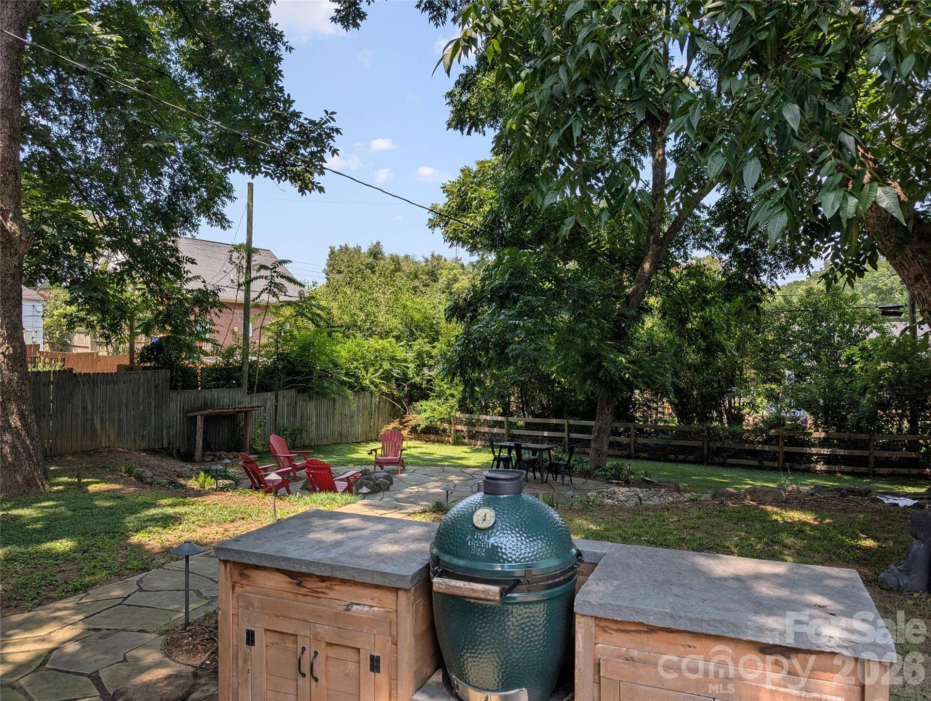 The outdoor kitchen features a Big Green Egg, cedar storage cabinets, and a dedicated prep surface, all overlooking the backyard retreat below.