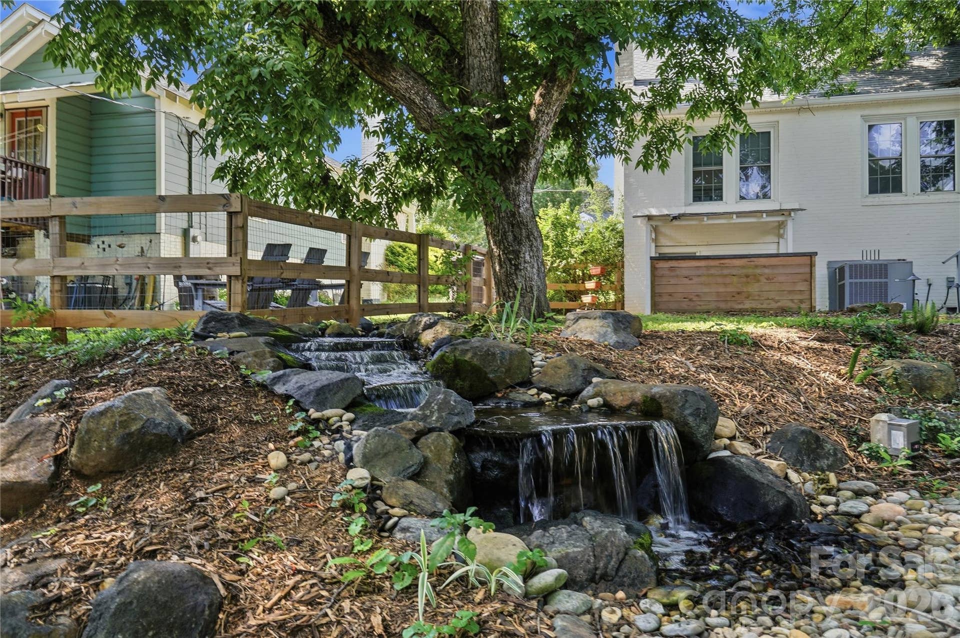 A tranquil waterfall feature, tucked beneath mature trees, brings a peaceful, resort-like feel to the backyard.
