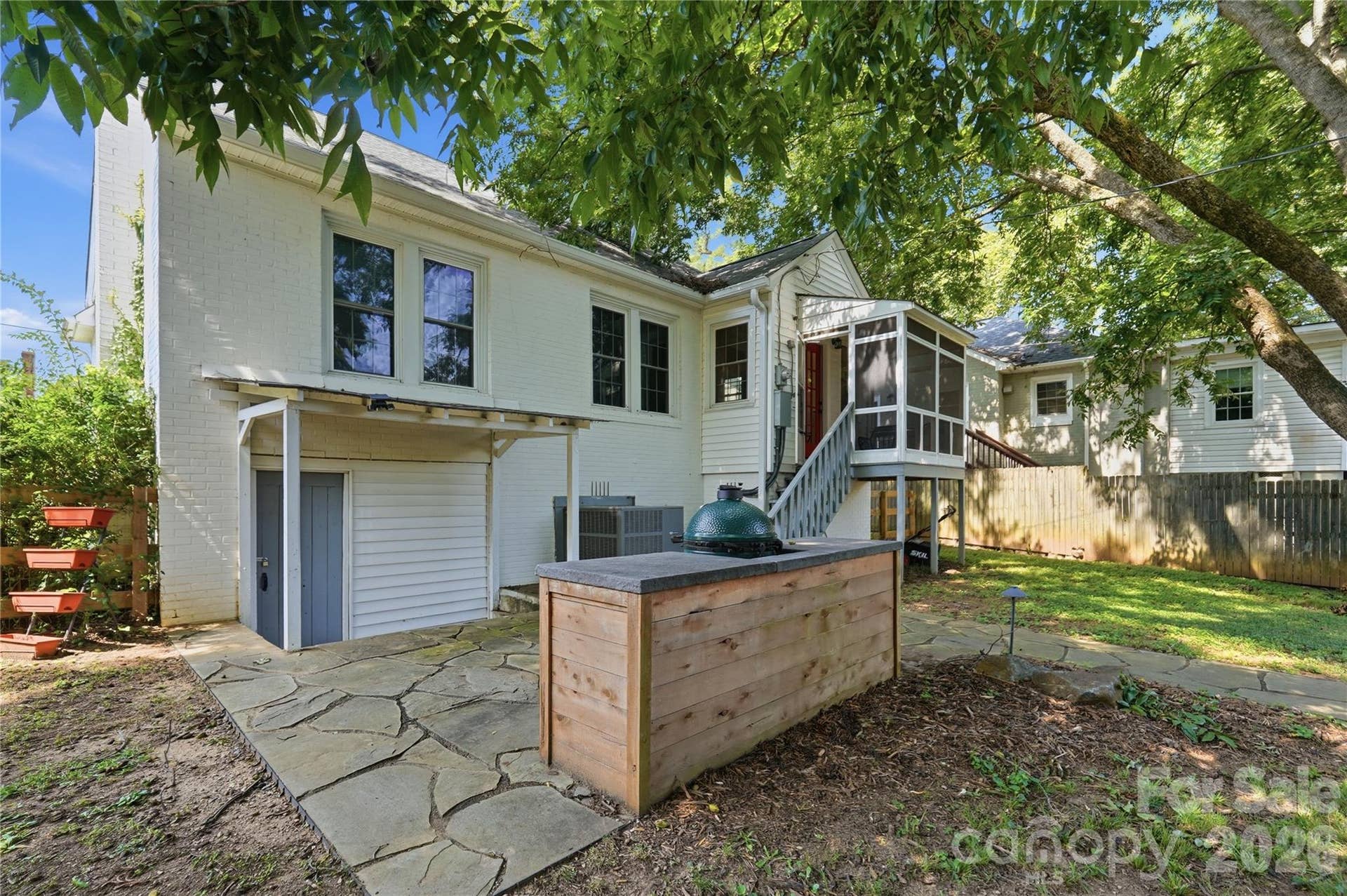 The screened porch connects seamlessly to the outdoor kitchen below, anchored by a Big Green Egg, with additional storage tucked beneath the home.