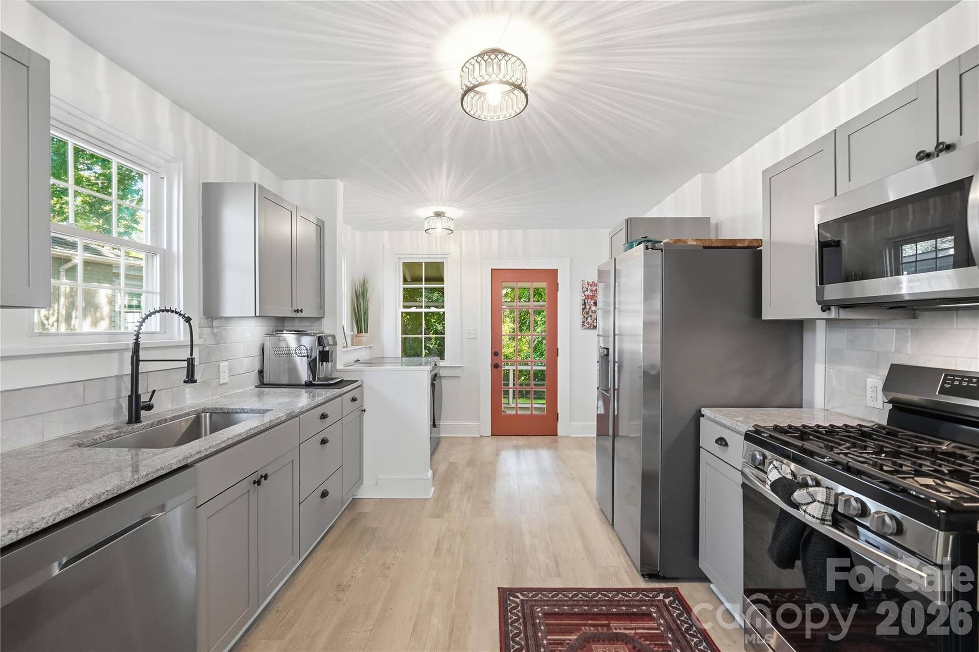 A fully renovated kitchen with granite countertops, gray shaker cabinets, and stainless steel appliances, all with a bright, open feel from wall to wall.