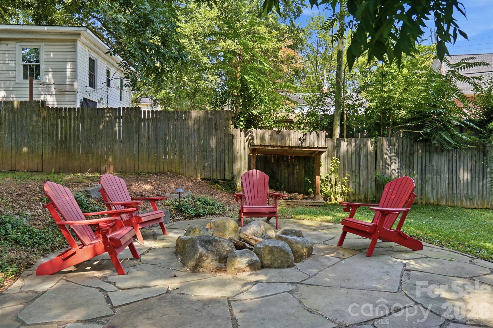 A stone fire pit surrounded by mature trees creates a cozy gathering spot for evenings outdoors.