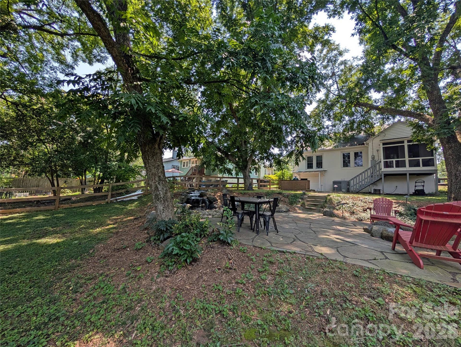 This patio sits beneath large trees, with a peaceful waterfall feature nearby and plenty of room for seating, whether you're relaxing solo or hosting a crowd.