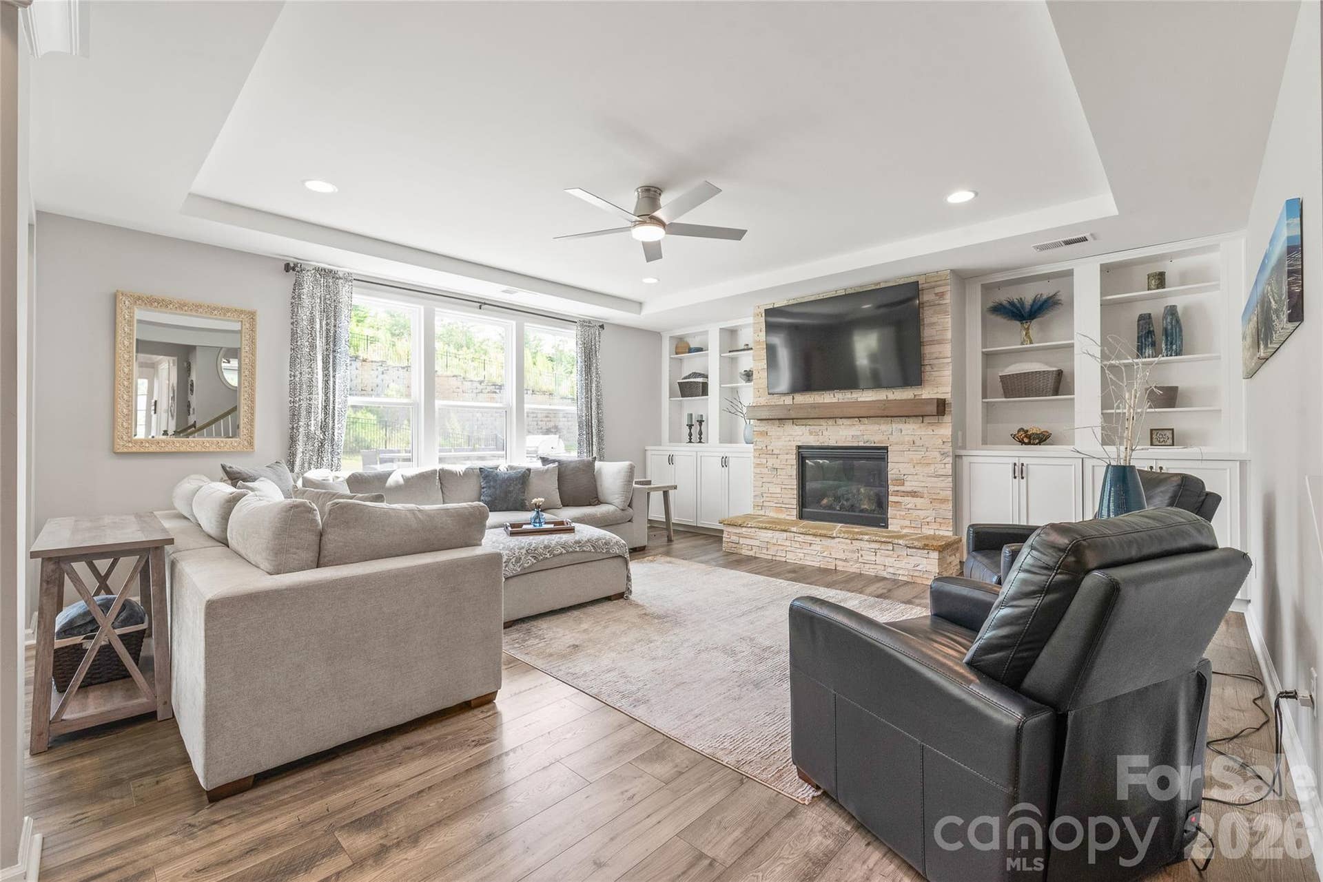 Anchored by a striking stone fireplace flanked by custom built-ins, the inviting living room offers a warm, spacious gathering spot bathed in natural light.