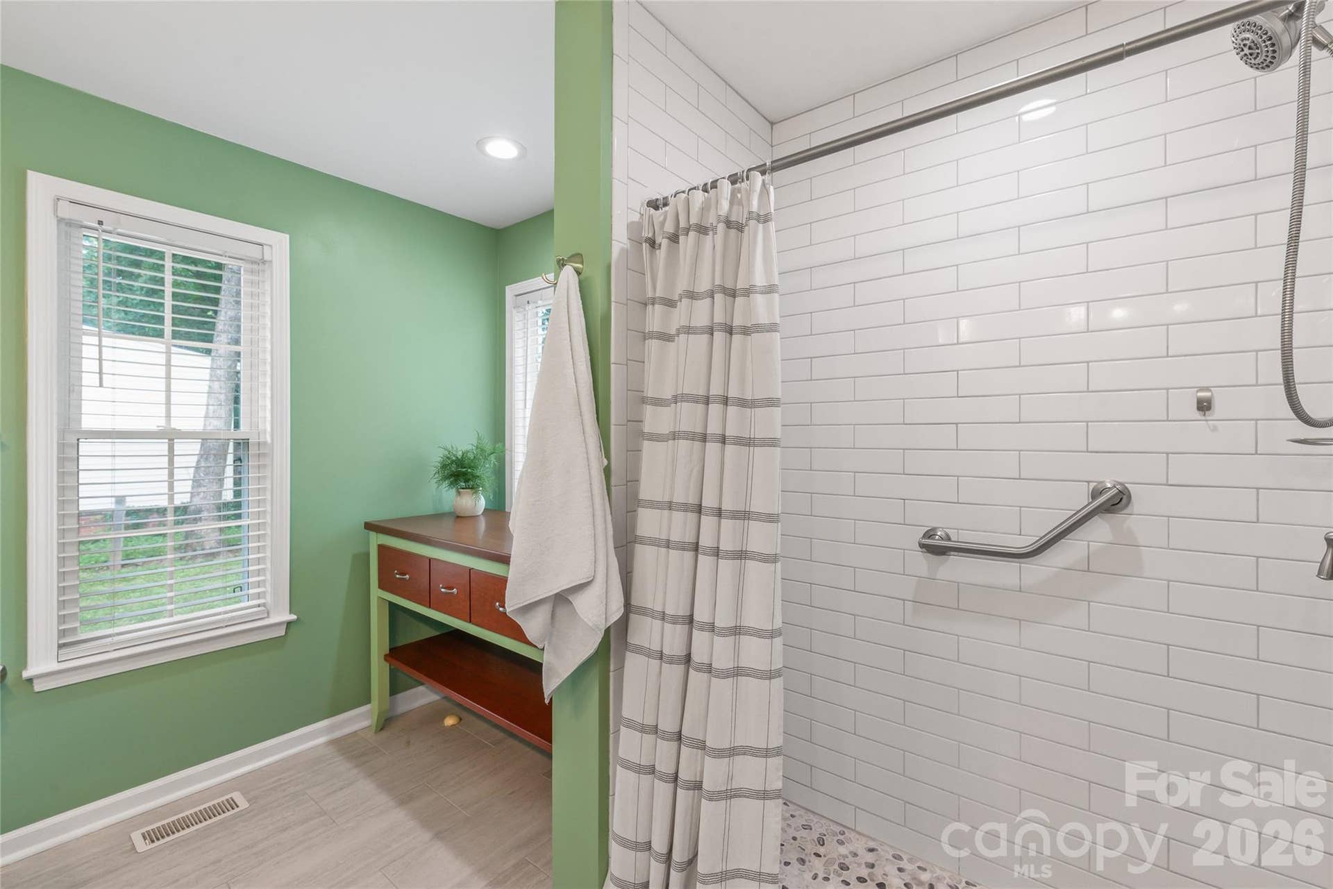 A spacious walk-in shower featuring a tile surround that extends all the way to the ceiling, plus dedicated space for a tub with plumbing neatly concealed beneath a custom furniture piece.