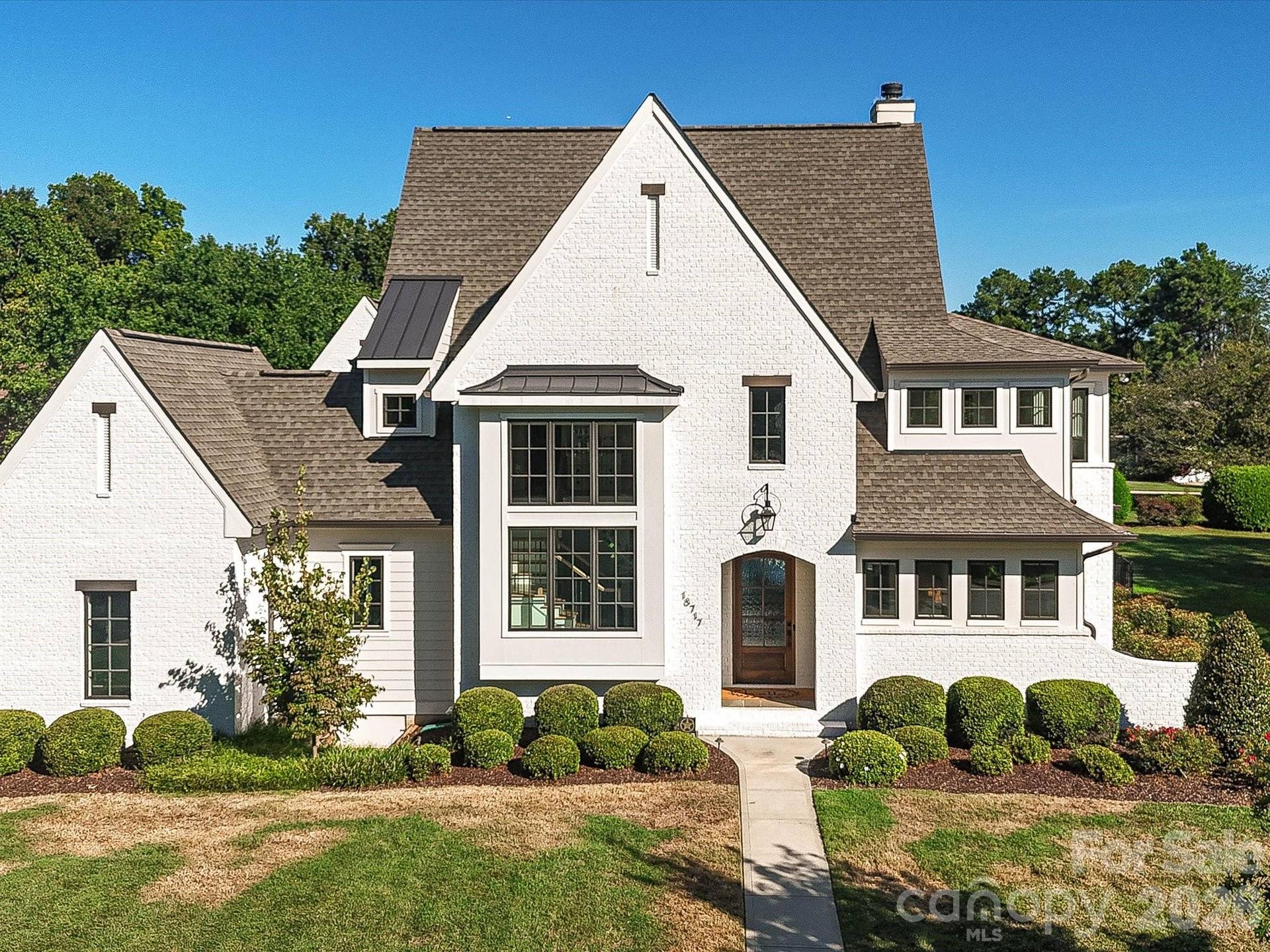 Impressive exterior showcases timeless white-brick architecture, manicured landscaping, and a spacious two-car garage with a broad driveway for convenient parking and access.