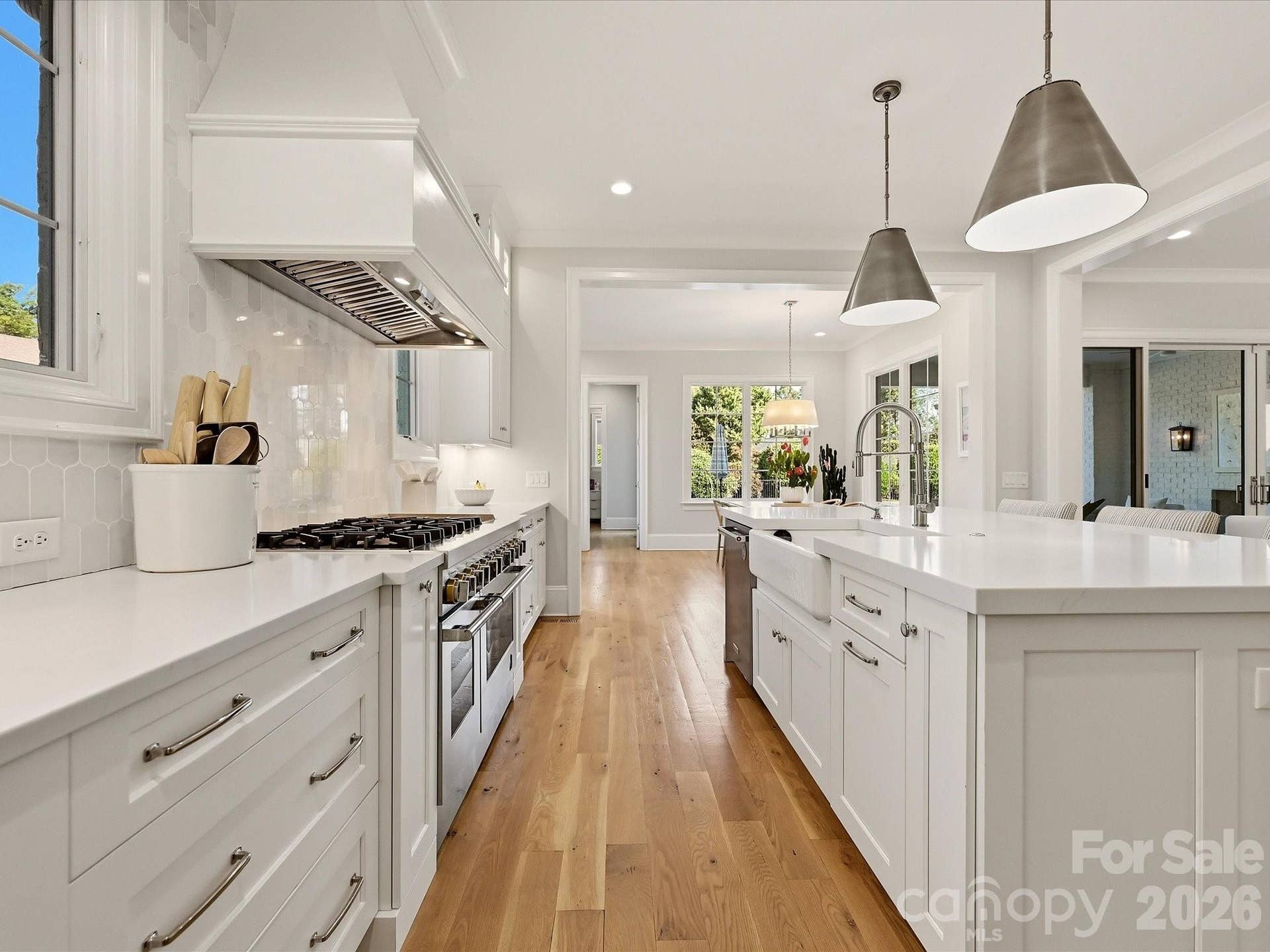 The kitchen flows effortlessly into a sunlit breakfast area, where expansive windows, hardwood floors, and views toward the covered patio create an inviting setting for casual dining.