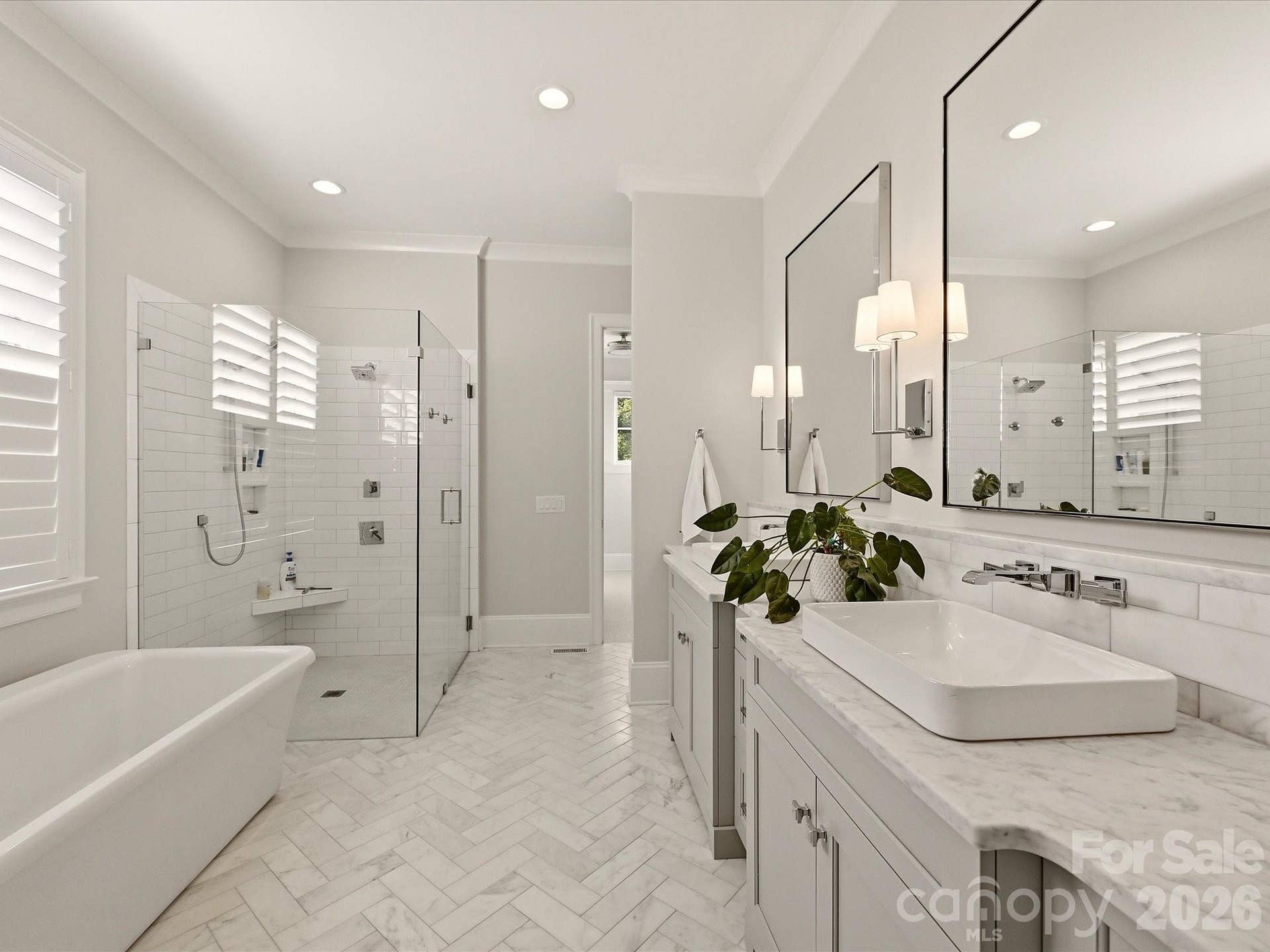 Spa-inspired Primary Bath features a freestanding soaking tub, oversized frameless glass shower, dual vanities with stone countertops, and elegant herringbone-patterned tile flooring.