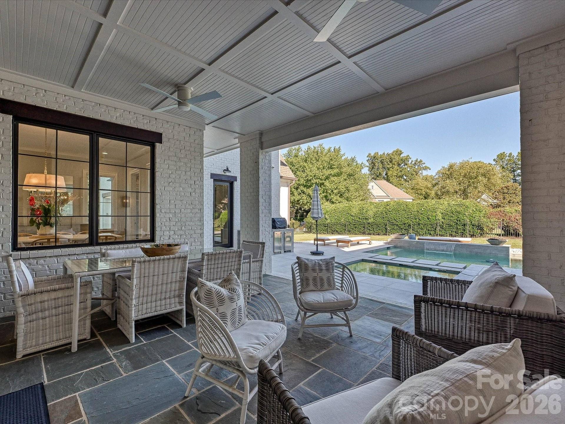 Expansive covered back patio extends the living space outdoors with a fireplace, ceiling fans, dining and lounge areas, and seamless access to the private pool.