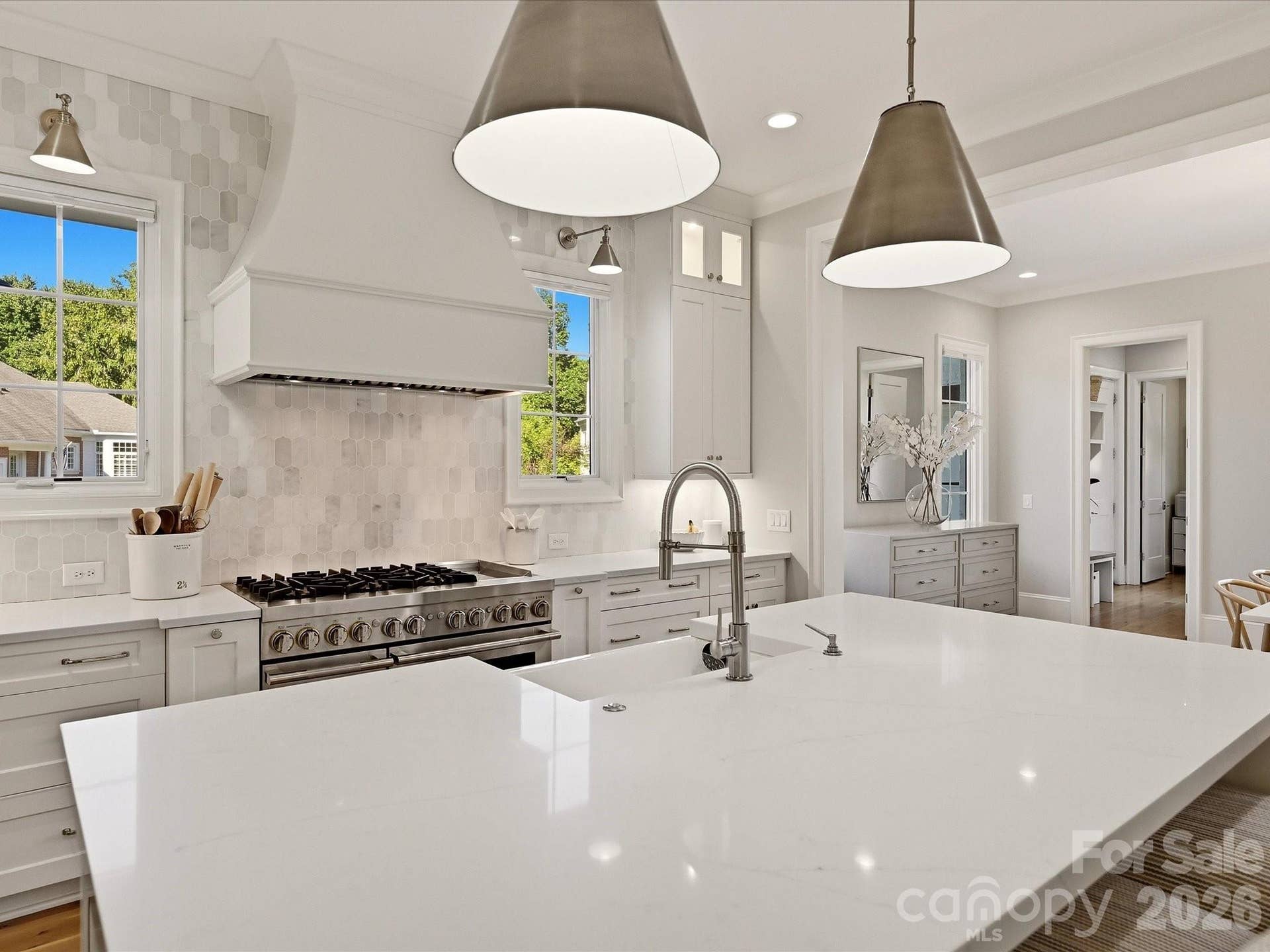 Bright designer kitchen features an oversized island with seating, custom cabinetry, stainless steel appliances, a statement range hood, beverage refrigerator, and abundant workspace for everyday living and entertaining.