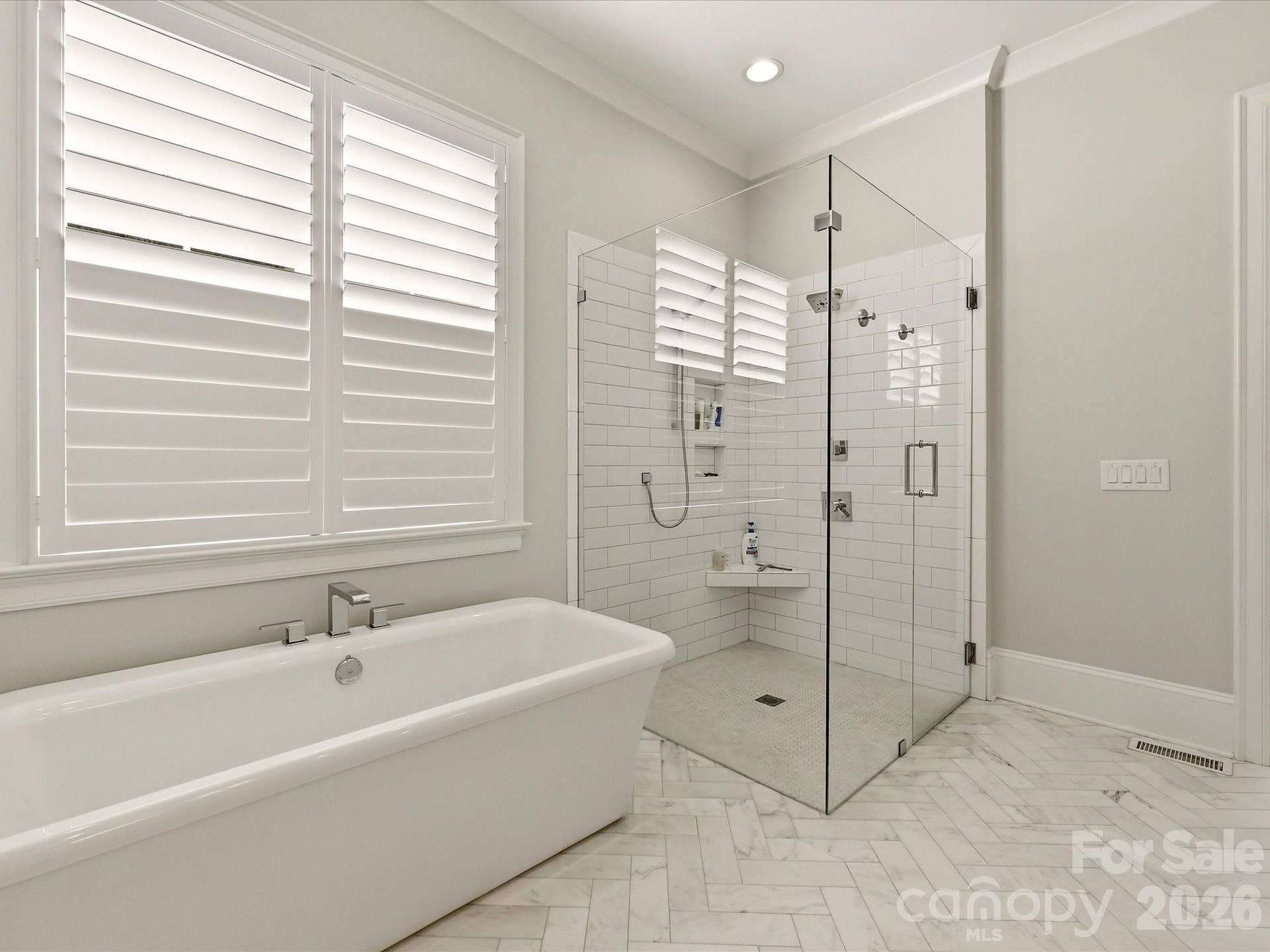 Spa-inspired Primary Bath features a freestanding soaking tub, oversized frameless glass shower, dual vanities with stone countertops, and elegant herringbone-patterned tile flooring.