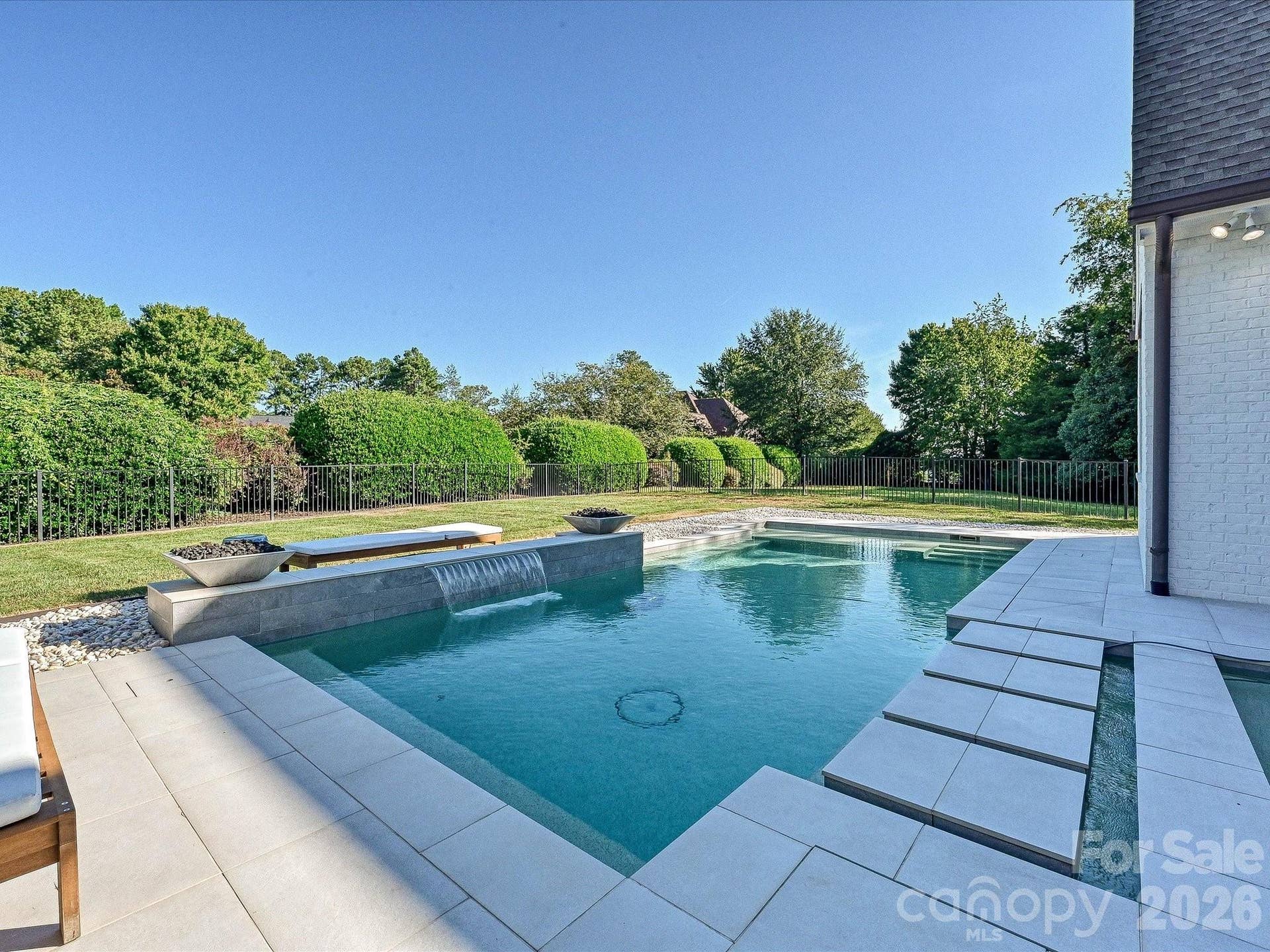 Resort-style backyard showcases a sleek, salt water, heated pool and spa with waterfall feature, expansive patio space, and a private setting ideal for outdoor entertaining and relaxation.