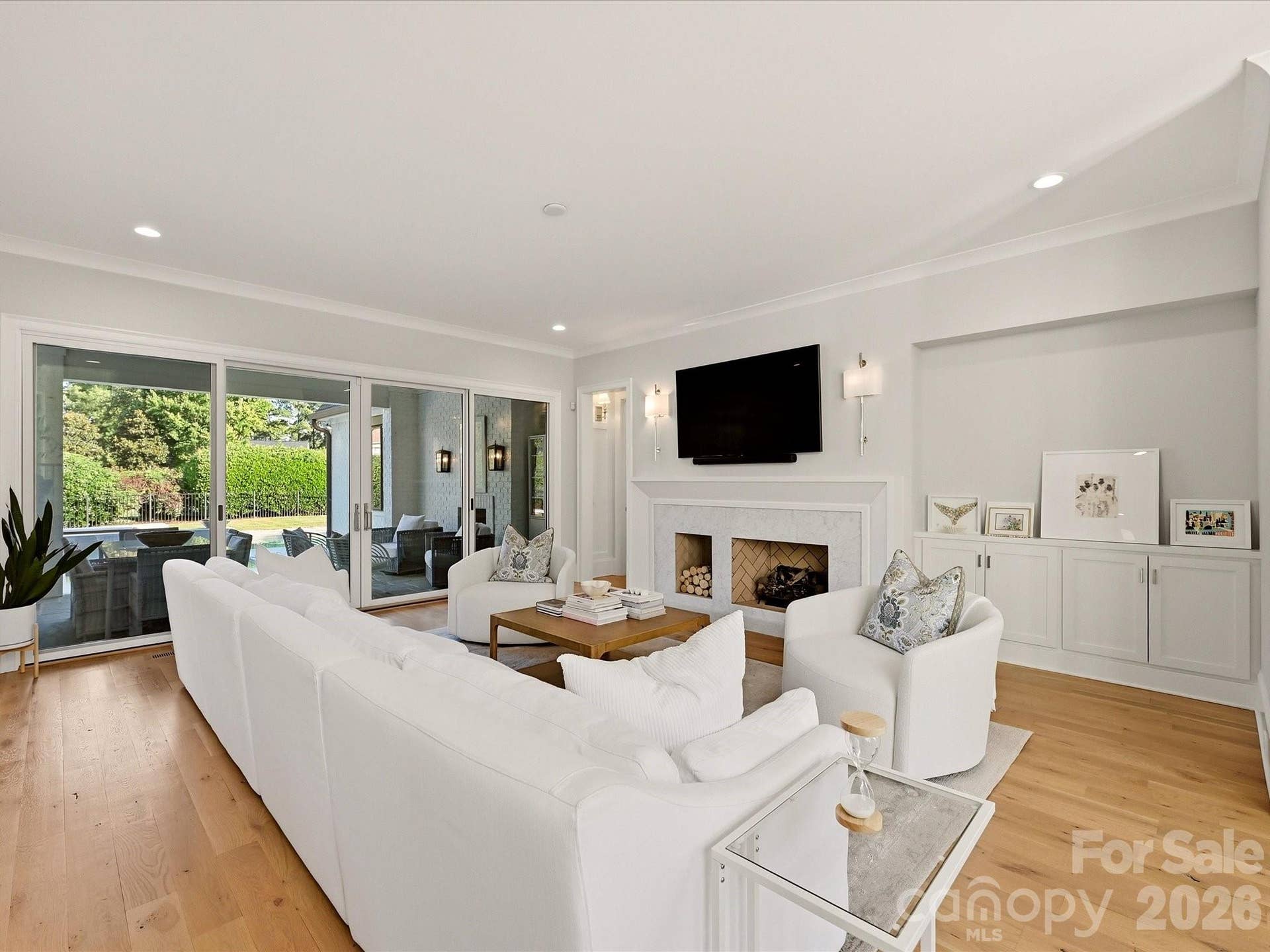 Light-filled Great Room features warm hardwood floors, a sleek fireplace with built-ins, seamless flow to the kitchen, and expansive glass doors opening to the covered outdoor living area.