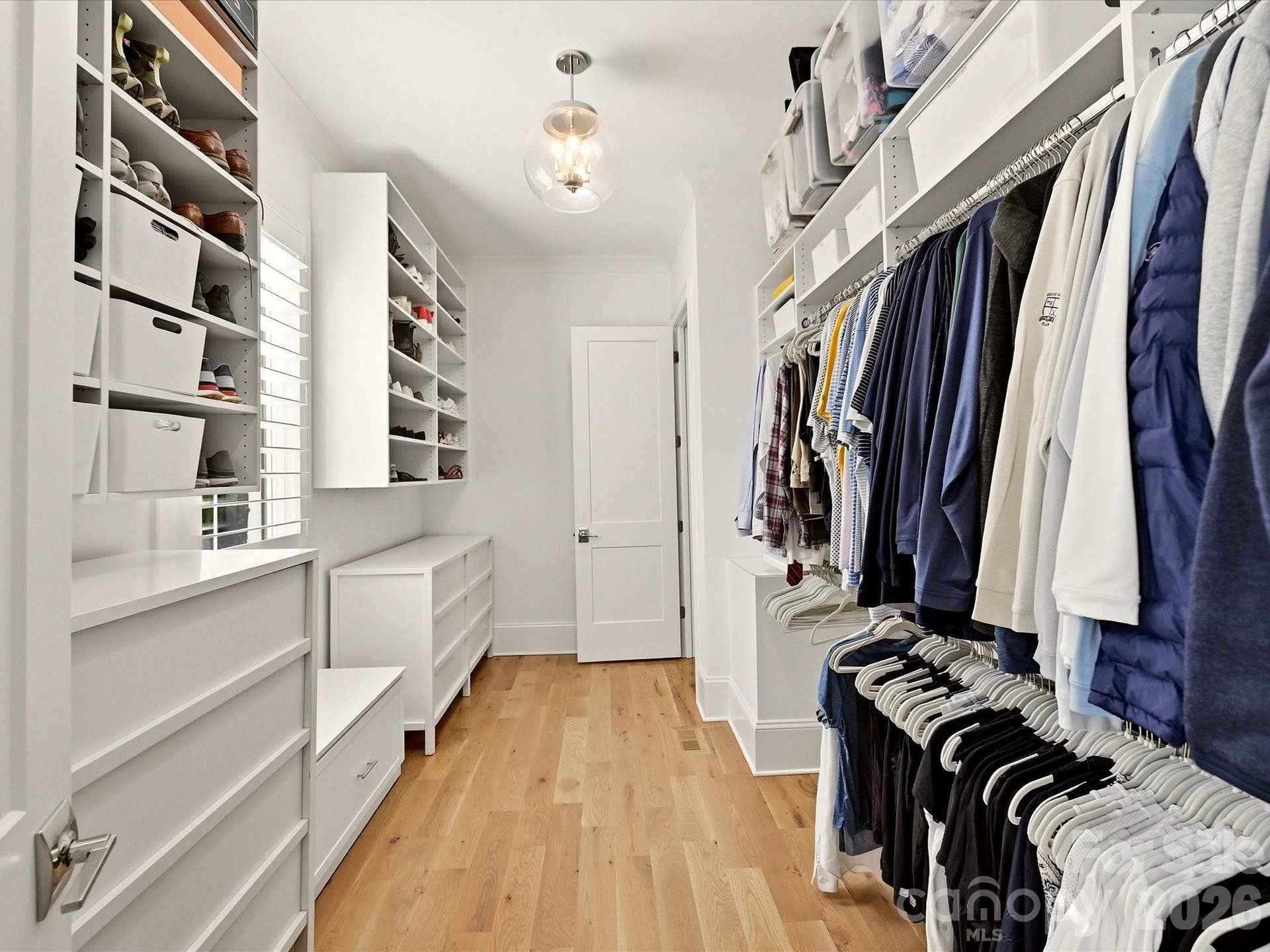 Expansive Primary walk-in closet offers custom built-in shelving, abundant hanging space, dedicated shoe storage, and hardwood floors for a beautifully organized retreat.