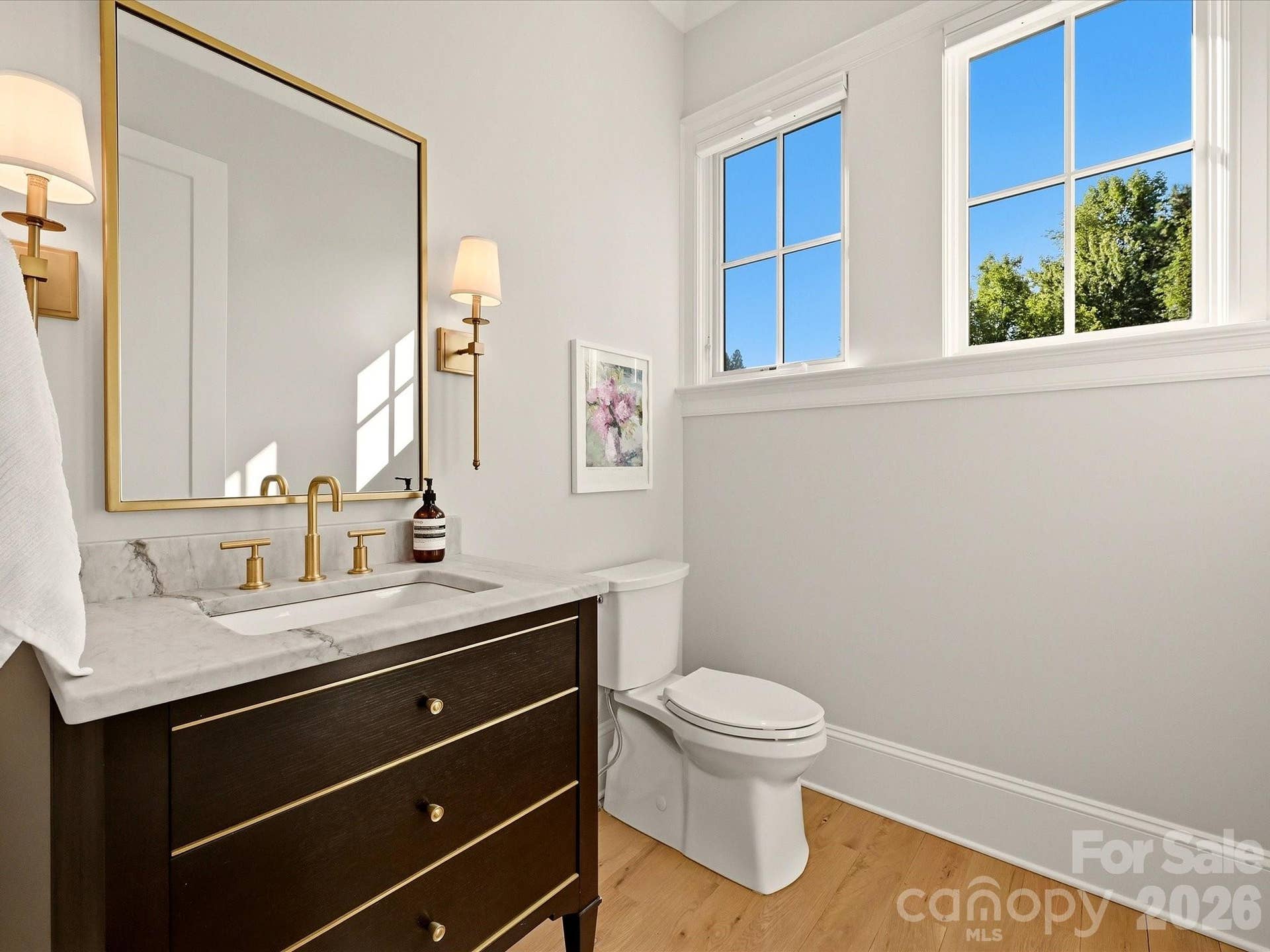 Stylish powder room features a furniture-style vanity with stone countertop, warm brass accents, hardwood flooring, and abundant natural light.