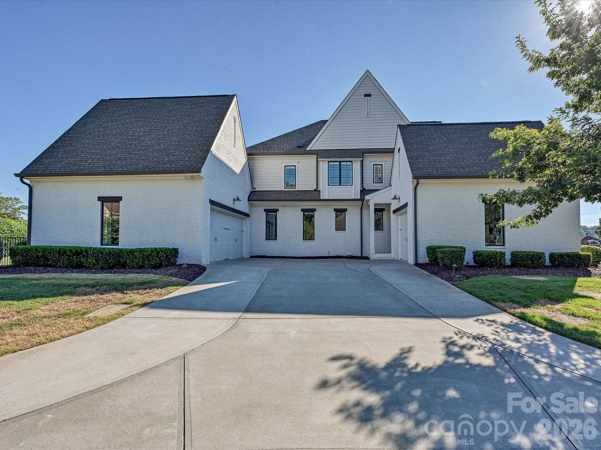 Impressive exterior showcases timeless white-brick architecture, manicured landscaping, and a spacious two-car garage with a broad driveway for convenient parking and access.