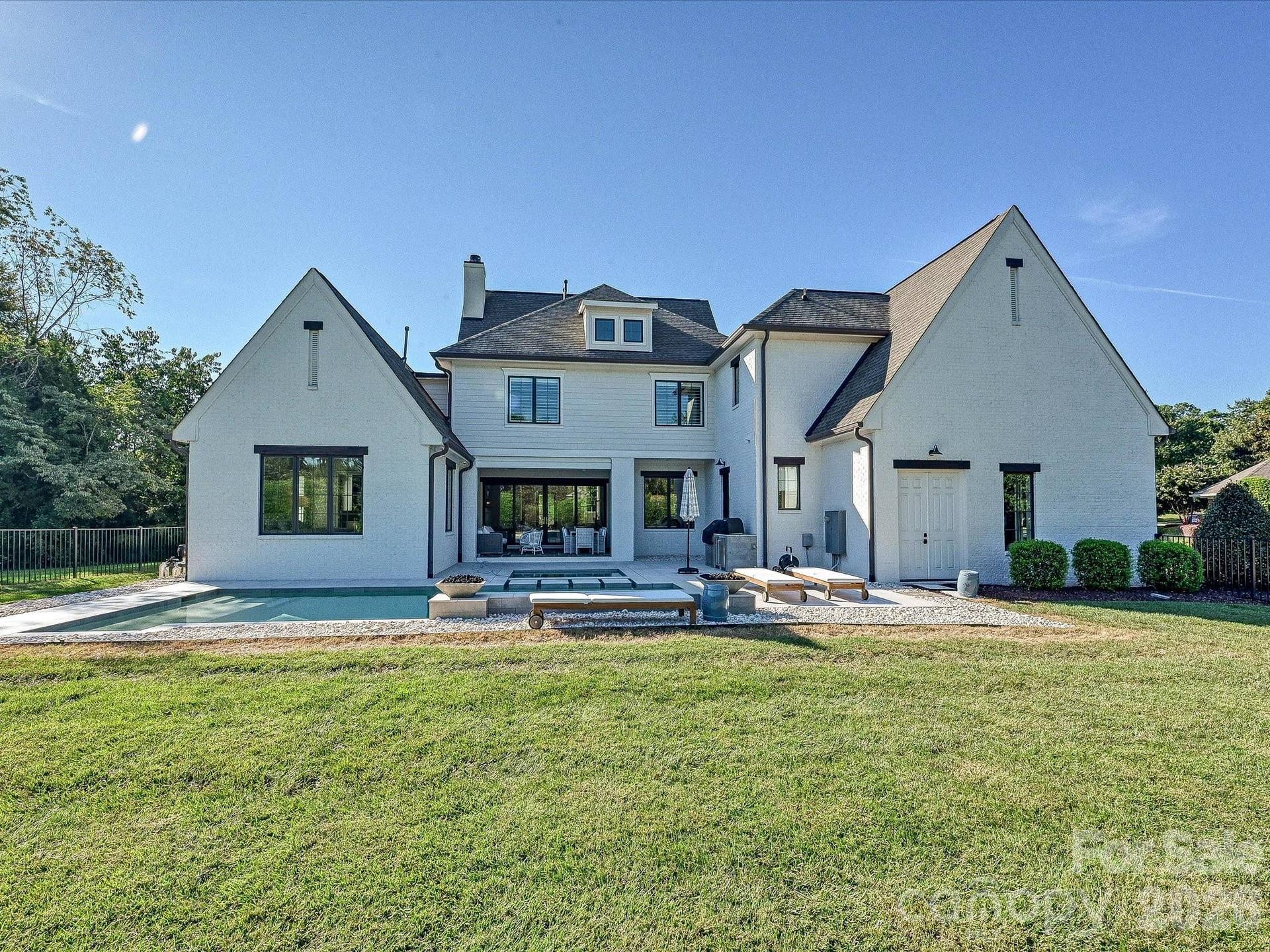 Rear exterior highlights the homes striking architecture, expansive lawn, covered patio, and seamless connection to the private pool and outdoor living areas.