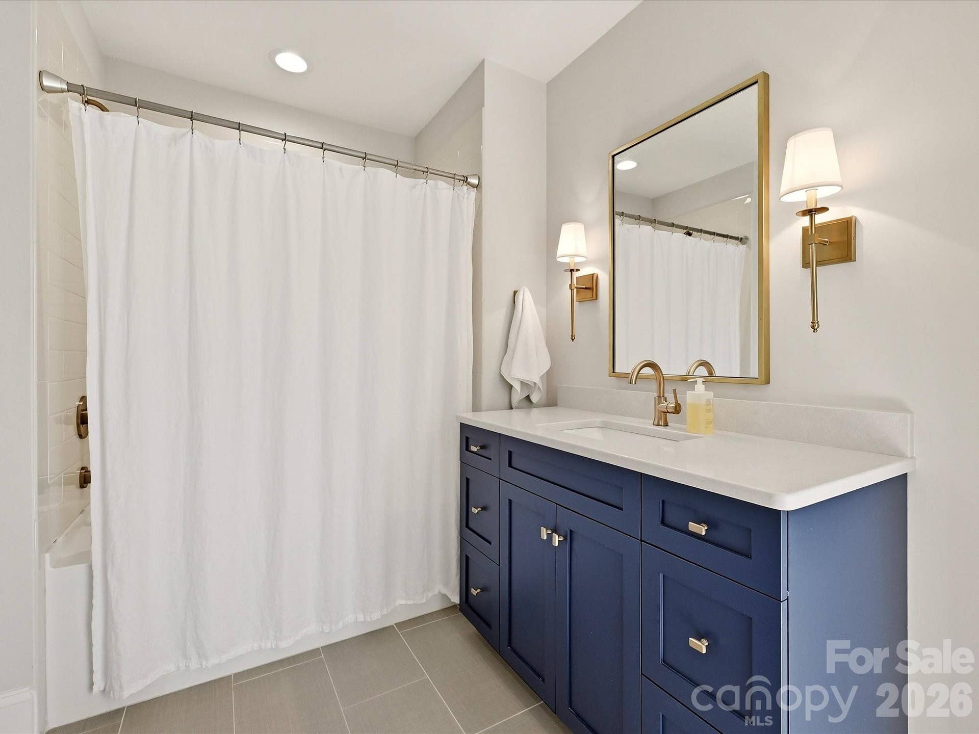 Stylish Jack-n-Jill  bath features a rich blue vanity, sleek countertop, warm brass accents, and a tub/shower combination with clean, modern finishes.