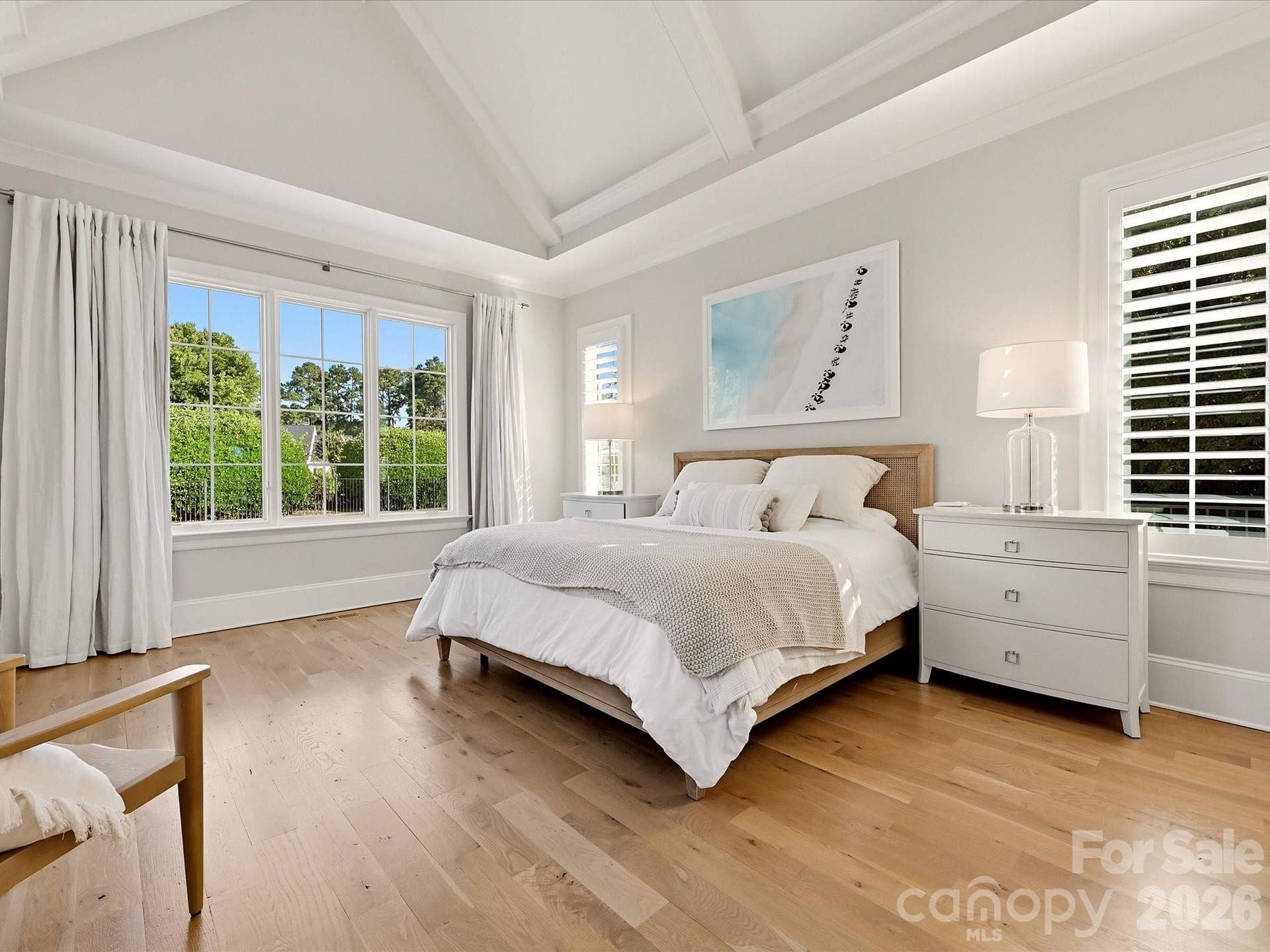 Spacious Primary Suite offers a vaulted ceiling with architectural detail, abundant natural light, warm hardwood floors, and a private entry to the adjoining closet and bath.
