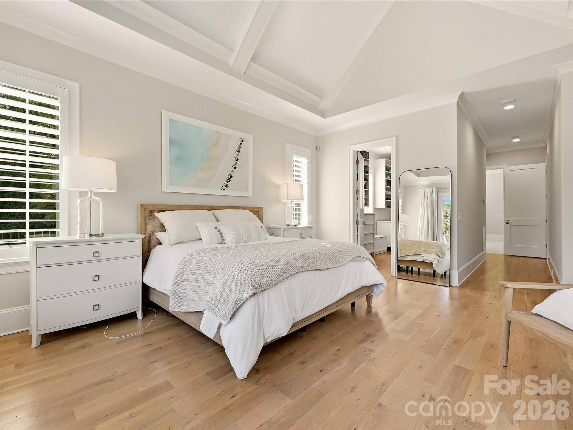 Spacious Primary Suite offers a vaulted ceiling with architectural detail, abundant natural light, warm hardwood floors, and a private entry to the adjoining closet and bath.