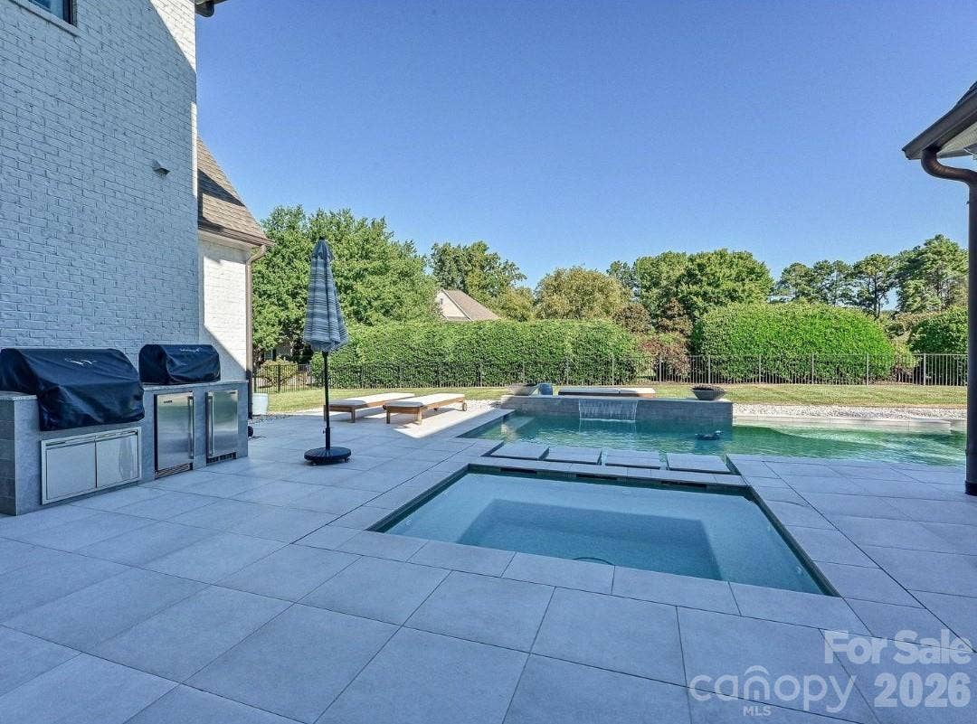 Resort-style backyard showcases a sleek, salt water, heated pool and spa with waterfall feature, expansive patio space, and a private setting ideal for outdoor entertaining and relaxation.