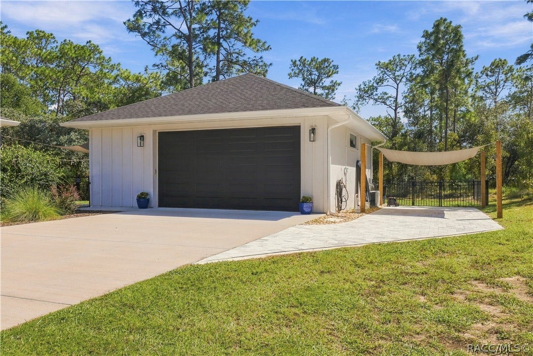 4124 W Pine Ridge Boulevard, Beverly Hills, FL 34465 DETACHED 30x30 GARAGE + PAVER PARKING AREA
Detached garage w/ coordinating board-and-batten-style exterior, contrasting dark garage door & exterior lighting. An extended paver area alongside the garage provides additional outdoor space, while the shade-sail setup & nearby fencing add extra function to the backyard.