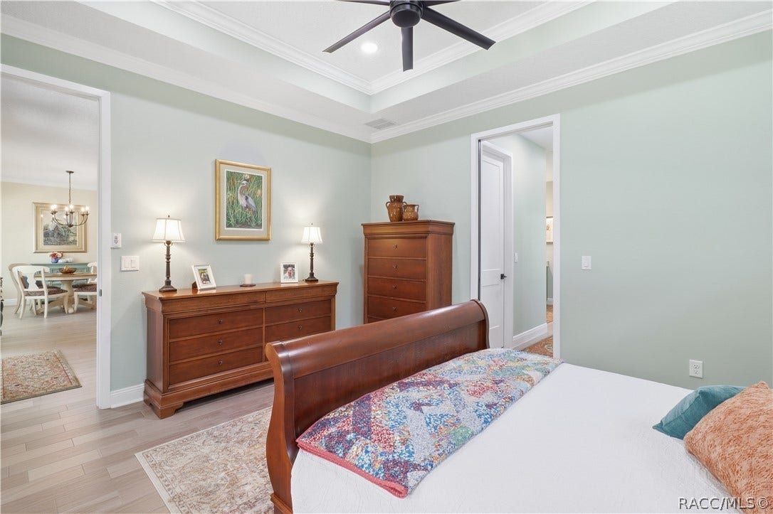 4124 W Pine Ridge Boulevard, Beverly Hills, FL 34465 PRIMARY BEDROOM Another view highlights the generous size of the primary suite, beautiful tray ceiling w/ layered crown molding, modern ceiling fan & porcelain tile flooring. Wide doorways provide easy access to the adjoining living area & private bath.