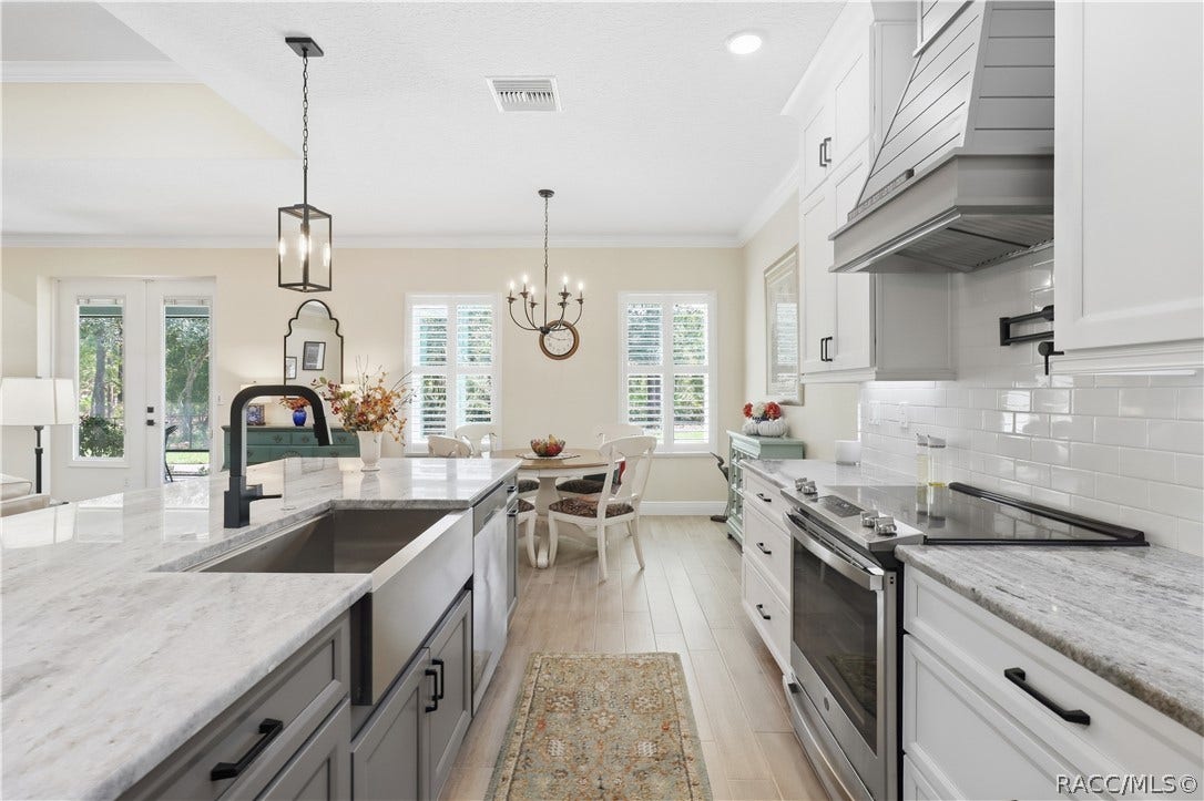 4124 W Pine Ridge Boulevard, Beverly Hills, FL 34465 KITCHEN DETAIL Crisp white cabinetry, subway-tile backsplash, stainless range, statement vent hood, pot filler, expansive counters & a large island create a polished, functional workspace.