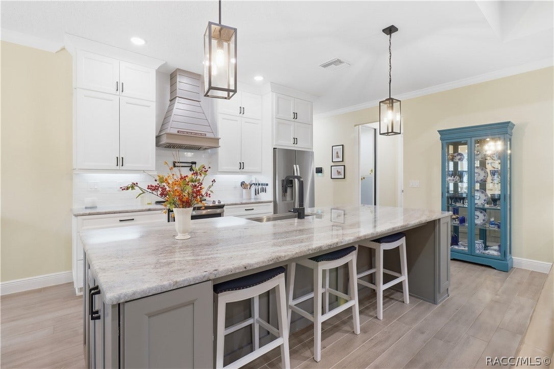4124 W Pine Ridge Boulevard, Beverly Hills, FL 34465 ENTERTAINER'S KITCHEN Extra-large island offers abundant seating, prep & serving space while tall cabinetry, stainless appliances, statement hood, pendant lighting & open sightlines elevate the room.
