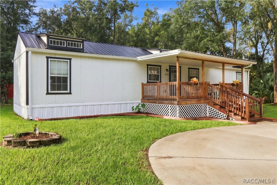 6230 W Glen Robbin Court, Crystal River, FL 34429 Front Exterior Attractive white exterior w/contrasting dark trim, METAL ROOF & spacious covered wooden porch, surrounded by a lush green lawn.