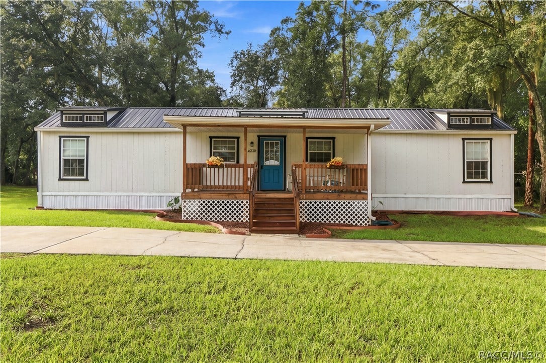 6230 W Glen Robbin Court, Crystal River, FL 34429 Front Elevation Enjoy the home's charming curb appeal, featuring a welcoming covered porch, wooden railings, decorative roof details & circular concrete driveway.