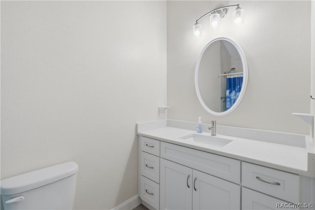 6230 W Glen Robbin Court, Crystal River, FL 34429 Primary Bathroom Bright bathroom featuring a white vanity w/solid-surface countertop, undermount sink, oval mirror, attractive lighting & convenient storage cabinetry.