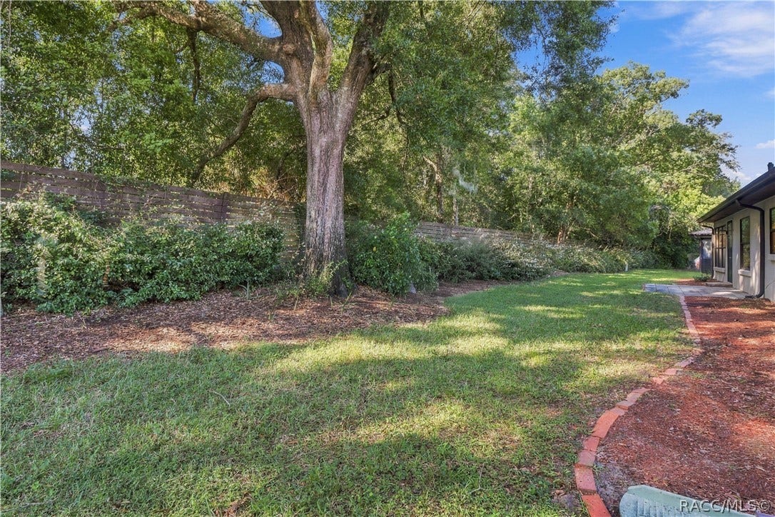 Beautifully landscaped backyard featuring mature shade trees, lush greenery, established shrubs, and a privacy-style fence along the rear boundary.