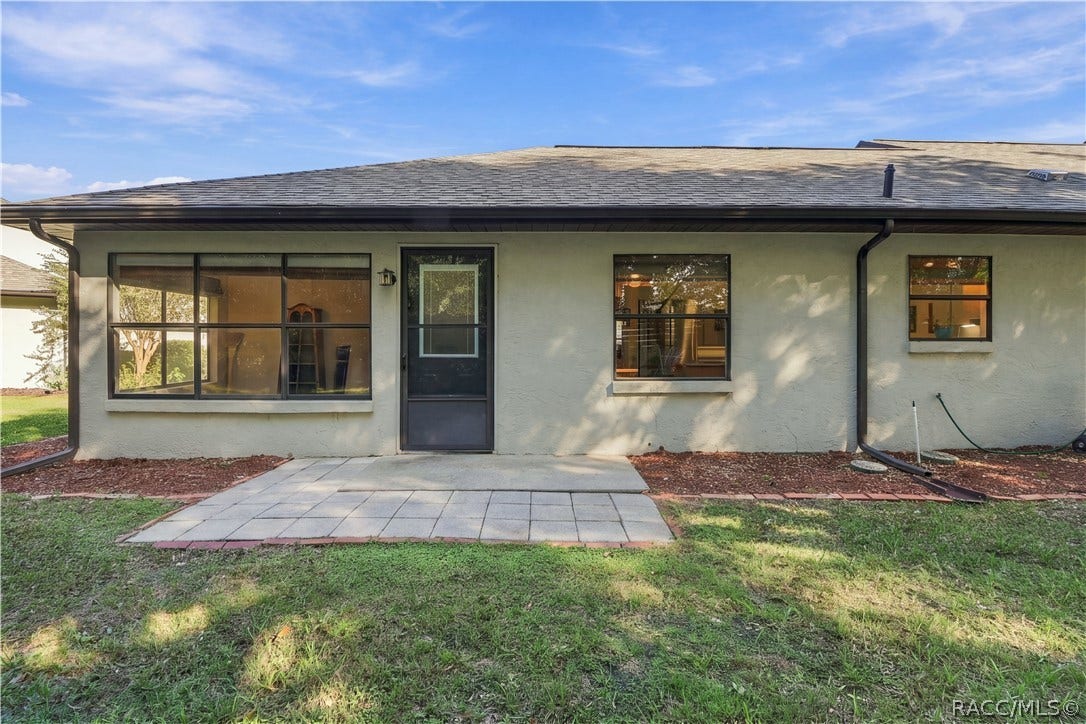 Rear exterior showcasing stucco construction, multiple windows, gutters, and a paved patio area.