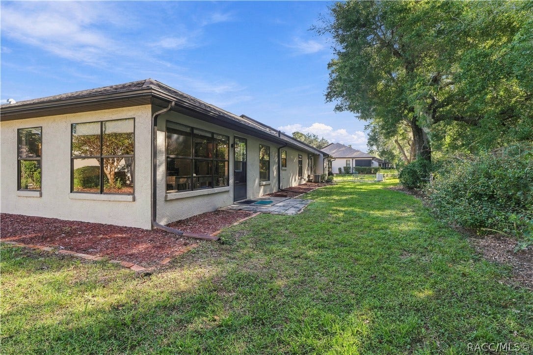 Side and rear exterior view showcasing the home's landscaping, grassy lawn, mature trees, and access to the enclosed porch.