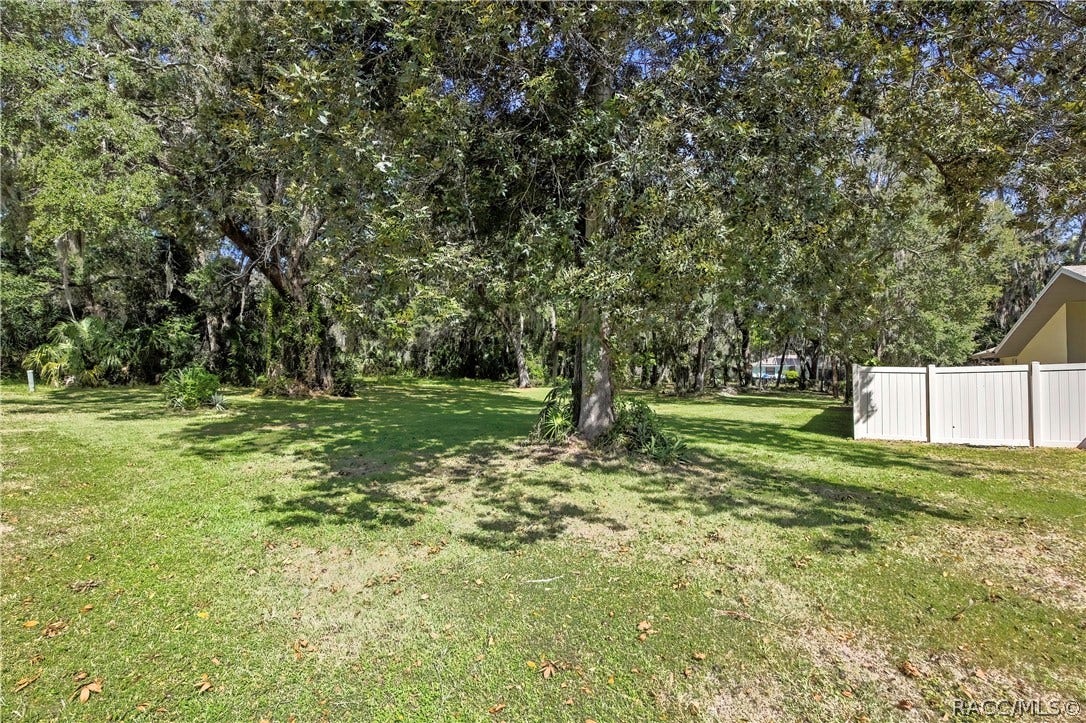 4737 S Sawmill Way, Homosassa, FL 34448 Grassy, tree-filled yard: palms, oaks with Spanish moss, chain-link fencing, and a stone bench at the right. No house in frame.