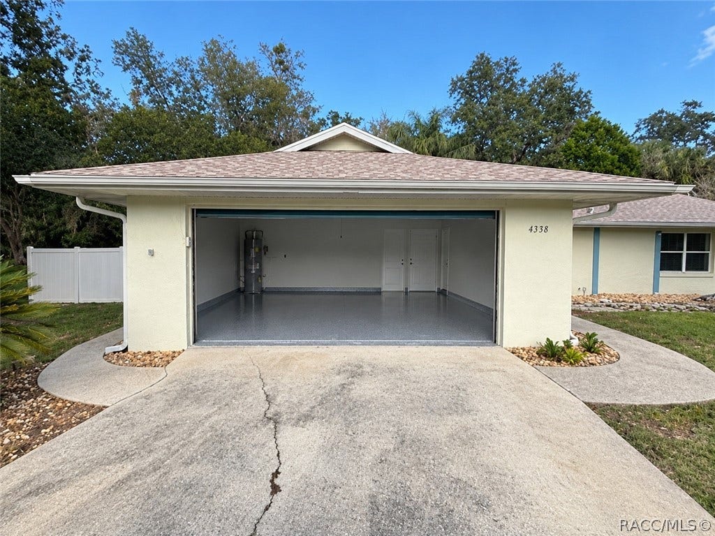 4737 S Sawmill Way, Homosassa, FL 34448 Clean, empty garage interior: smooth grey painted concrete floor, a white sectional garage door with metal rails and a garage door opener, a fluorescent tube light, a textured ceiling, beige walls, and a light wood empty shelving unit with two bays and four shelves against the back wall. No mower, boxes or clutter in this shot this is a different, newer garage photo than the two cluttered garage shots in the old set.